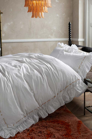 Lifestyle image of the White Mega Frill Duvet Cover and Pillowcase Set styled on a bed in a bedroom with various home accessories.