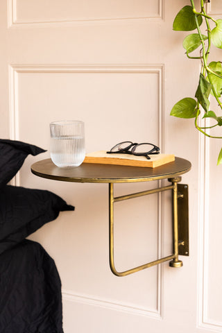 The Metal Table & Wall Shelf styled next to a bed, with a water glass, book and some glasses on, next to a plant.