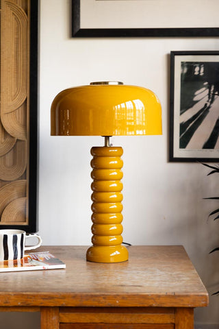 Lifestyle image of the Modern Metal Mustard Table Lamp displayed on a wooden desk surrounded by various other home accessories.