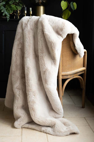 The Natural Faux Fur Throw displayed draped across a wicker chair, with candles and greenery in the background.