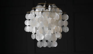 Tiered ceiling light comprising of chains of translucent white discs, displayed in front of a black panelled wall. 