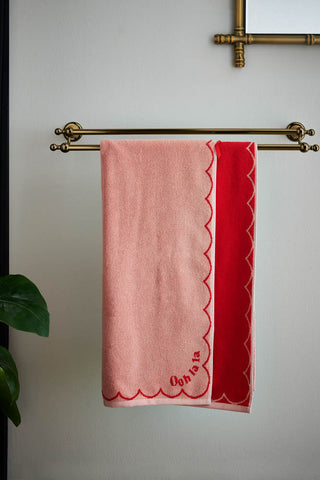 The Ooh La La Bath Towel displayed on a towel rail on a bathroom wall, next to a mirror and plant.