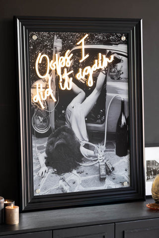 The Oops I Did It Again...Framed Neon Wall Light with a black frame styled on a black sideboard.