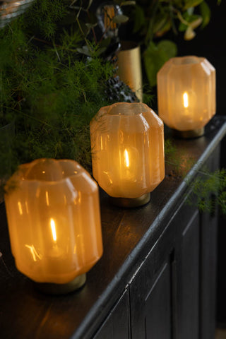 Three of the Orange & Gold Battery Powered Table Lamps displayed illuminated on a black sideboard surrounded by greenery.