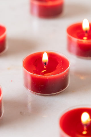 Close-up of some of the Pack of 20 Tealight Candles in Deep Red, lit and displayed on a white surface.