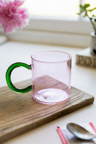 The Pale Pink & Green Glass Mug on a wooden board, surrounded by various accessories.