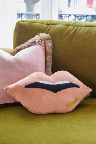 Lifestyle image of the Pink Lips Cushion on a green sofa.