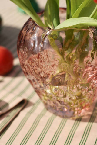 Lifestyle image of the Pink Strawberry Glass Vase displayed on a striped tablecloth and styled with flowers inside. 