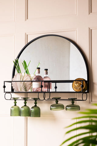 Beautiful black framed arched mirror with a shelf and hanging racks for glassware. The bar shelf is styled with pink fizz, cocktail glasses and cocktail stirrers.