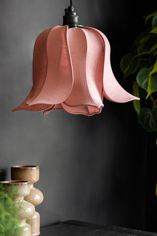 The Pretty Pink Petal Leaf ceiling light shade in front of a dark wall, styled with greenery and candlestick holders.
