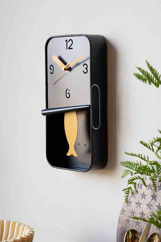 The Quirky Sardine Tin Pendulum Wall Clock on the wall, styled above various accessories and a plant.