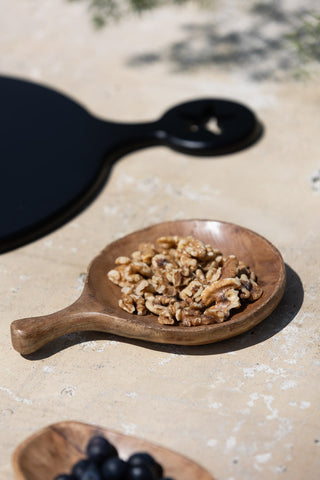 The Round Natural Wood Carved Serving Dish on an outdoor table in the sunshine, styled with walnuts inside.