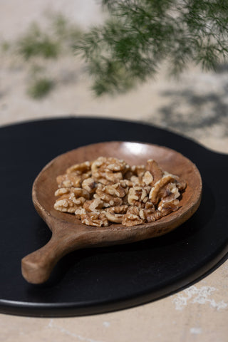The Round Natural Wood Carved Serving Dish on top of a black serving board, styled with walnuts inside.