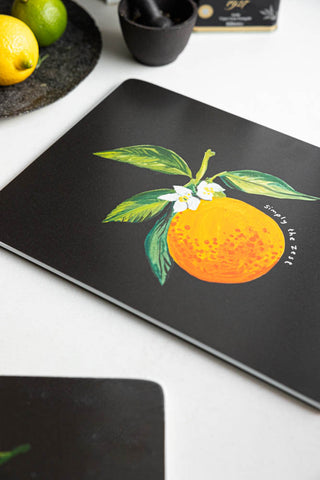 Close-up image of the Orange Placemat, with fruit and kitchen accessories also in the shot. 