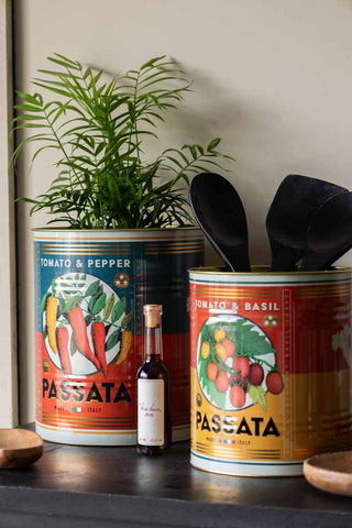 The Set Of 2 Passata Storage Tins - Large displayed together on a black sideboard, styled with a plant and kitchen accessories.