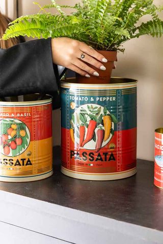 The Set Of 2 Passata Storage Tins on a sideboard with a plant being placed inside.