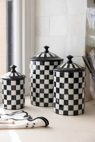 The Set Of 3 Enamel Black & White Check Tins displayed together on a kitchen window ledge, styled with a napkin and other kitchen accessories.