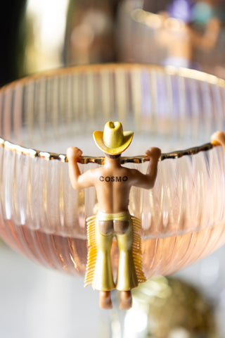 A yellow cowboy drink marker on the edge of a glass with the word 'cosmo' on the back.