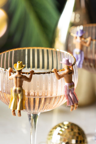 Two cowboy drinks charms hanging onto the edge of a cocktail glass.