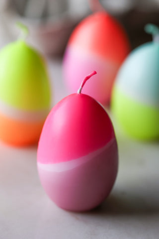 Lifestyle image of the Set Of 4 Neon Dip Dye Egg Candles displayed on a white surface. 