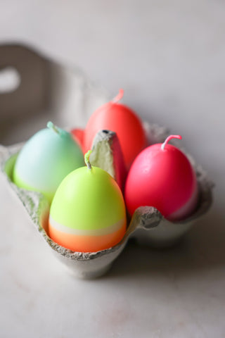 Lifestyle image of the Set Of 4 Neon Dip Dye Egg Candles displayed in a box on a white surface. 