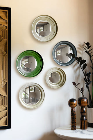 The Set Of 5 Metal Frame convex mirror set in Green & Natural displayed on a neutral wall next to a framed artwork and a table with some ornaments and a potted plant on.