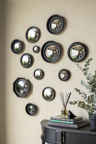 The Set of 12 Black Convex Mirror set displayed on a neutrall wall above a console table styled with various home accessories.