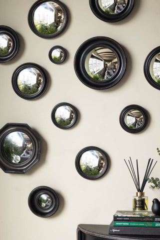 Close-up of the Set of 12 Black convex mirror set styled on a wall, above a table with some books, a diffuser, a bird ornament and a plant.
