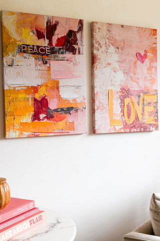 A styled image of the Set of 2 Pink & Orange Abstract Peace/Love Wall Art on a white wall.