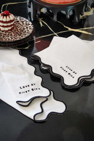 Lifestyle image of the Set of 4 Black & White First Bite Napkins styled on a black surface next to leopard print side plates.