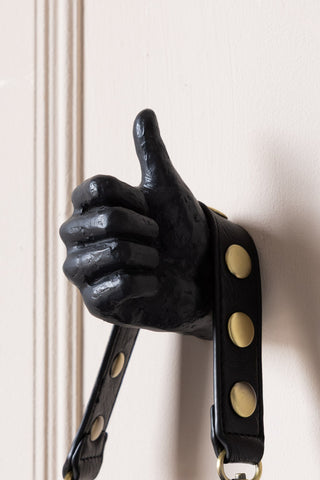 A thumbs up hand wall hook with a bag hanging from it.