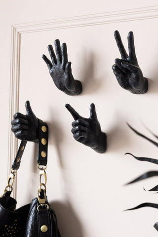 Four hand wall hook styled on the wall with a bag, next to a plant.