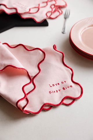The Set of 4 Pink & Red First Bite Napkins displayed on a table with a fork, plate and serving board.