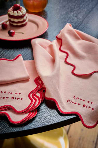Lifestyle image of the Set of 4 Pink & Red First Bite Napkins on a black wooden table.