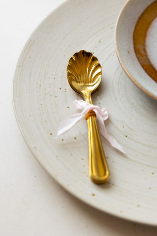 One of the Set of 4 Gold Shell Teaspoons styled on a plate with a bow.