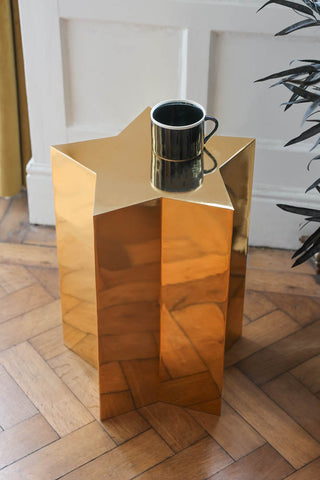 Lifestyle image of the Shiny Gold Star Side Table styled with a mug and next to a plant. 