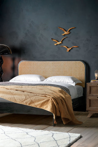 The Sleek Curved Wooden Bedframe styled with pillows and a throw on, with a black floor lamp, bird wall decorations and a bedside table with accessories on.
