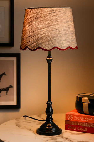 Lifestyle image of the Slim Table Lamp with Red Scalloped Linen Shade illuminated and displayed on a marble table with other home accessories.