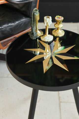 Lifestyle image of the Small Black Star Side Table styled with candlesticks on the top. 