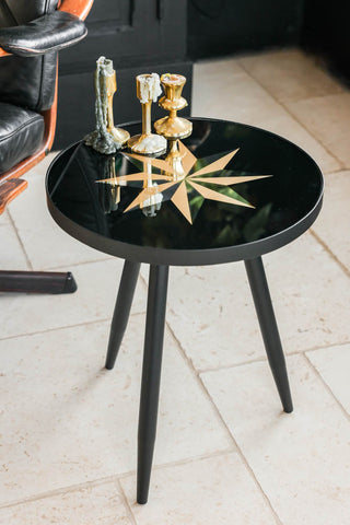 Lifestyle image of the Small Black Star Side Table styled with candlesticks on the top. 