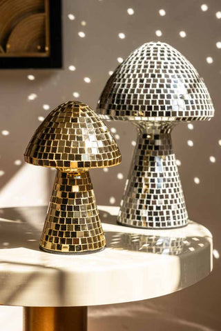 The Small and Large Disco Mushroom Ornaments displayed together on a table in the sunshine, reflecting light onto the wall in the background.
