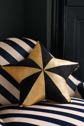 Lifestyle image of the Black & Gold Star Cushion on a striped armchair.