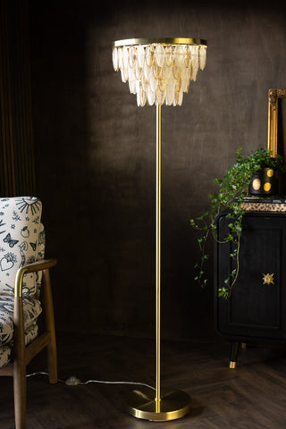 The Stunning Art Deco Glass Feather Floor Lamp styled next to a patterned amrchair and a sideboard with a plant and a gold frame on.