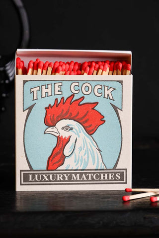 Lifestyle image of The Cock Luxury Matches displayed on a black tabletop. 