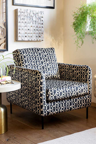 The Edie Daisy Print Velvet Armchair styled in the corner of a room with a side table, accessories, plants and artwork.