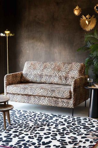 A styled image of the The Edie Leopard Print 2 Seater Sofa styled next to a leopard print rug and plants.