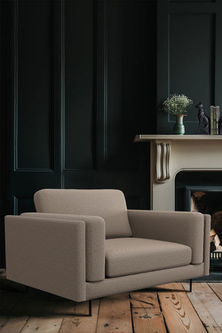 The Grace Love Seat In Studio Stripe Velvet Sand & Black styled in a dark room in front of a fireplace, with various home accessories on.
