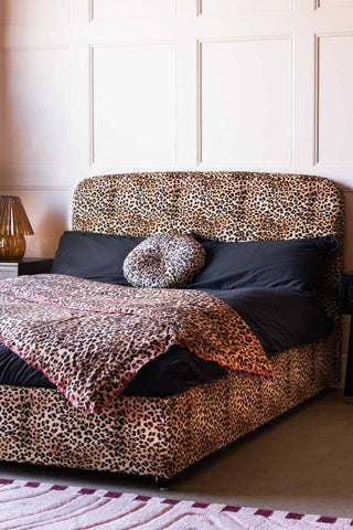 The Jagger Bed in Leopard Love Velvet styled with a cushion and throw on, next to some bedside tables and a lamp.