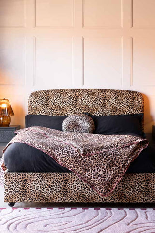 The Jagger Bed in Leopard Love Velvet styled with a throw and cushion on, with some bedside tables and an amber lamp.