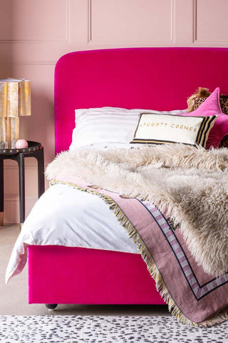 A close up image of the The Jagger Bed in Luxe Needlecord Velvet Harry's Pink with a black side table next to it.